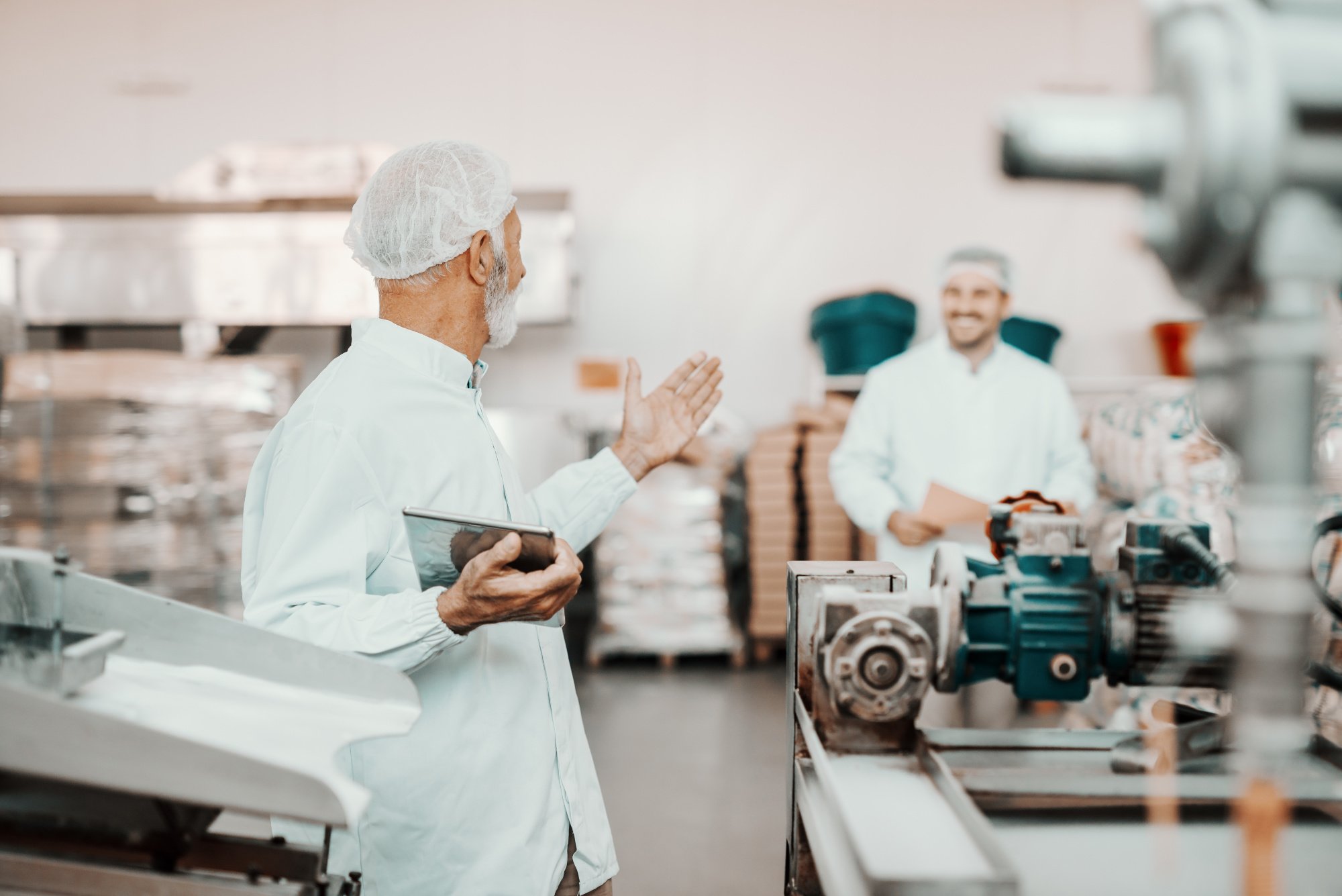 Employees in sanitary gear talking in an industrial kitchen.